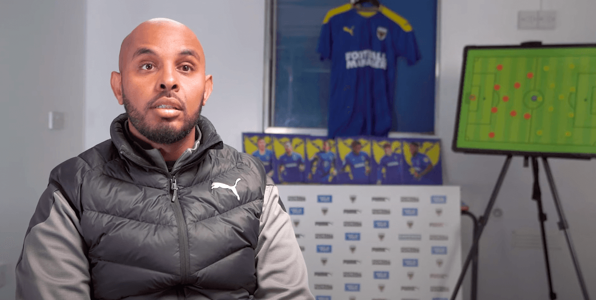 Coach from AFC Wimbledon sits in front of camera during an interview in coaching room.