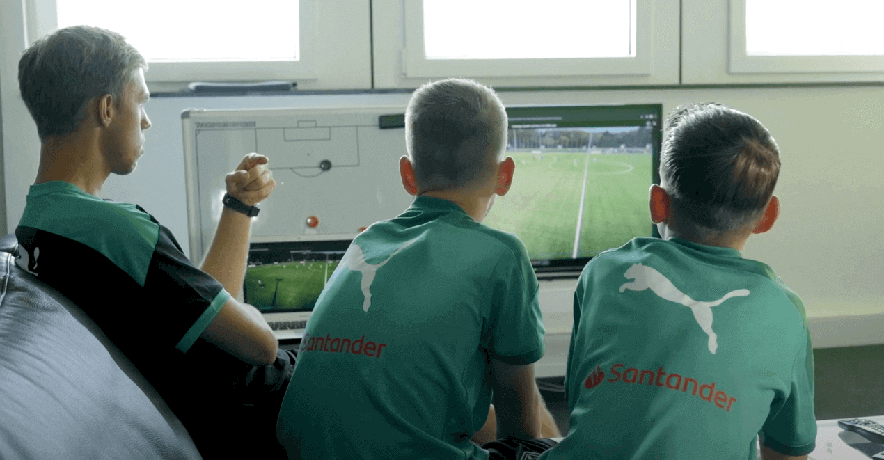 Three people, including a coach and two young soccer players, are viewing a video recording of their match captured by a Veo soccer camera